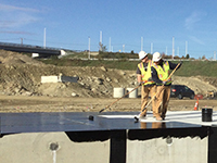 Workers use rollers to apply membrane layer